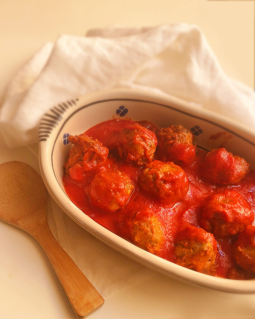 meatballs with tomato sauce in a pan, with a napkin and a wooden spoon