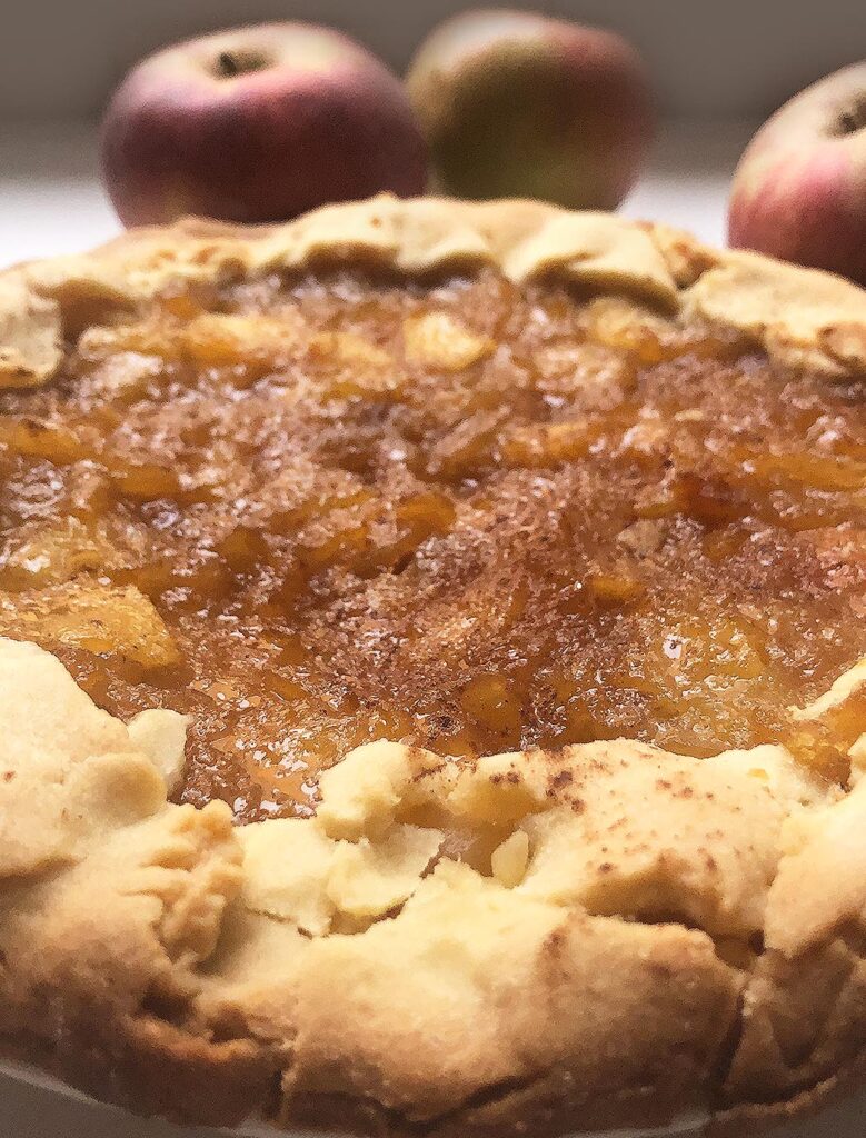 close up of "crostata" cake with caramelized apples with apples fruit on the background