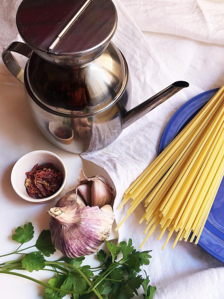 spaghetti on a blue dish, garlic, parsley chili pepper and a oil bottle itlaian cooking tips