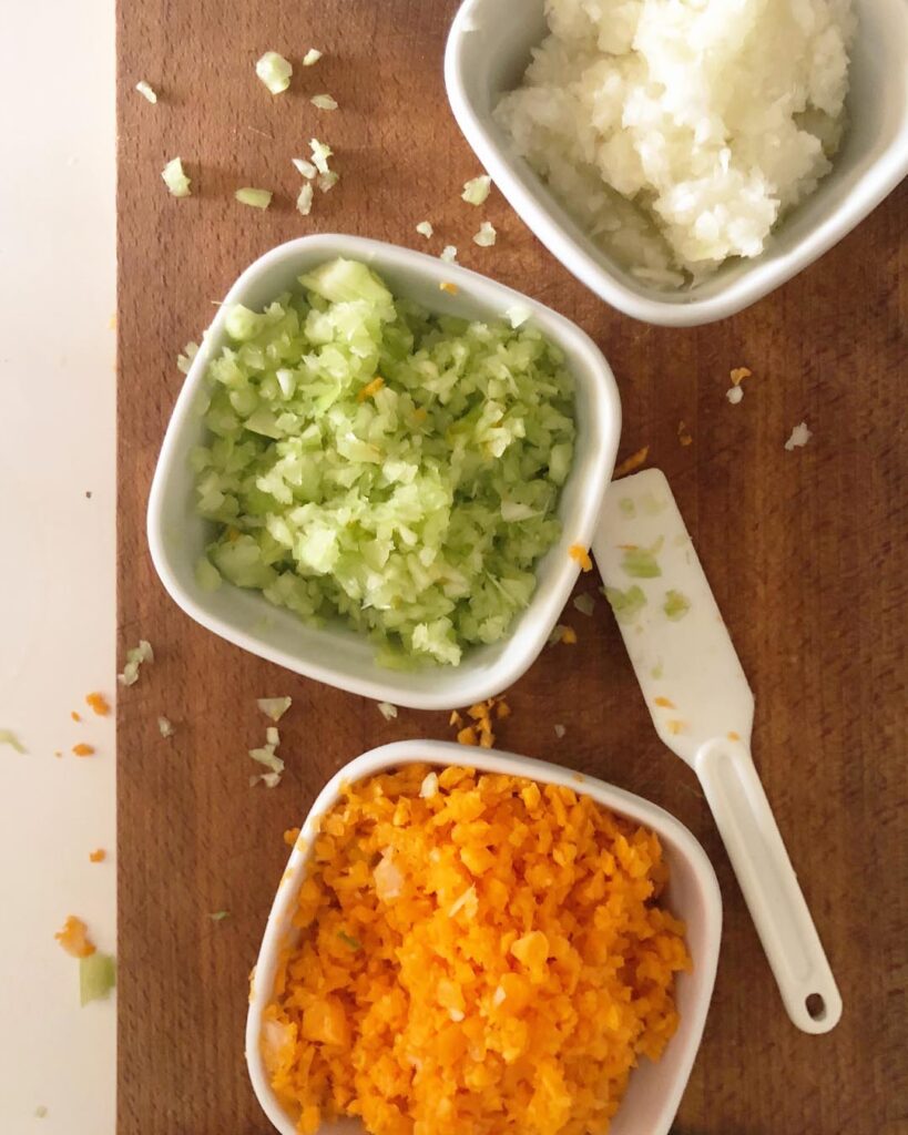 3 pans on a chop board with chopped onions, celery and carrots