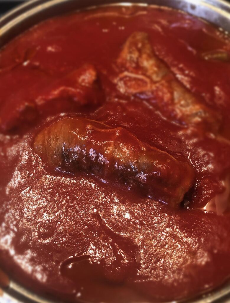 meat rolls cooking into a pan with tomato sauce