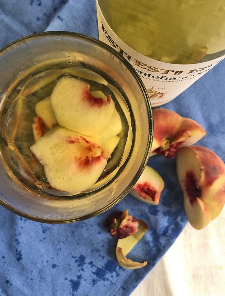 a glass of white wine, a bottle of wine and a peach