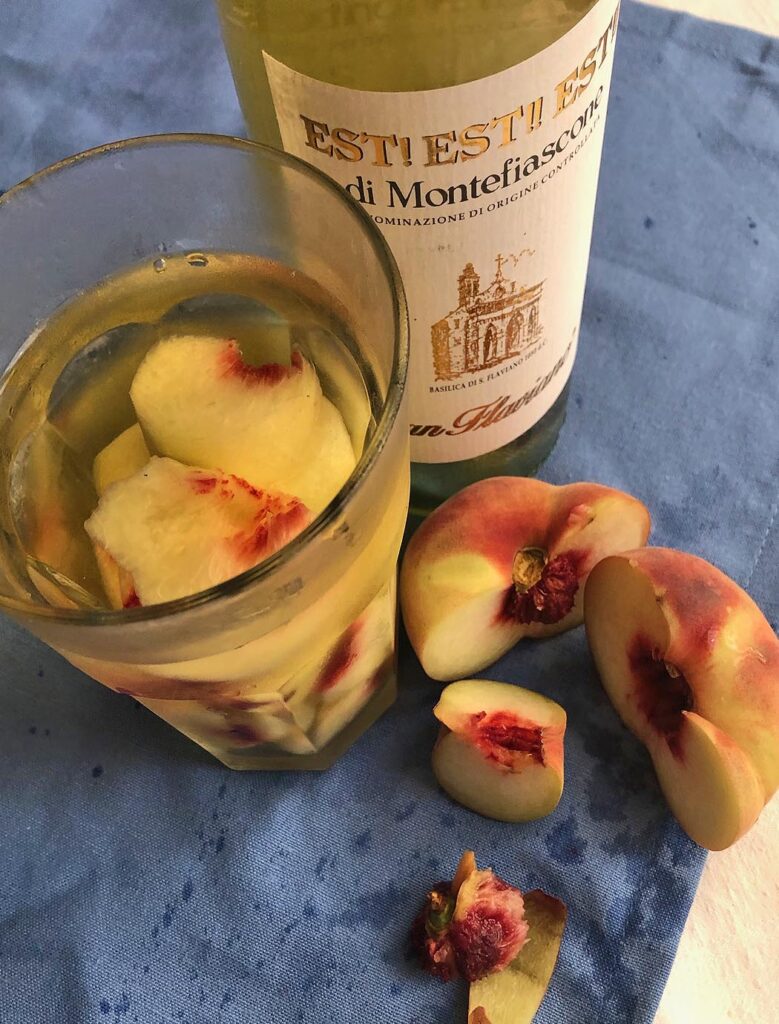 a glass of white wine, a bottle of wine and a peach