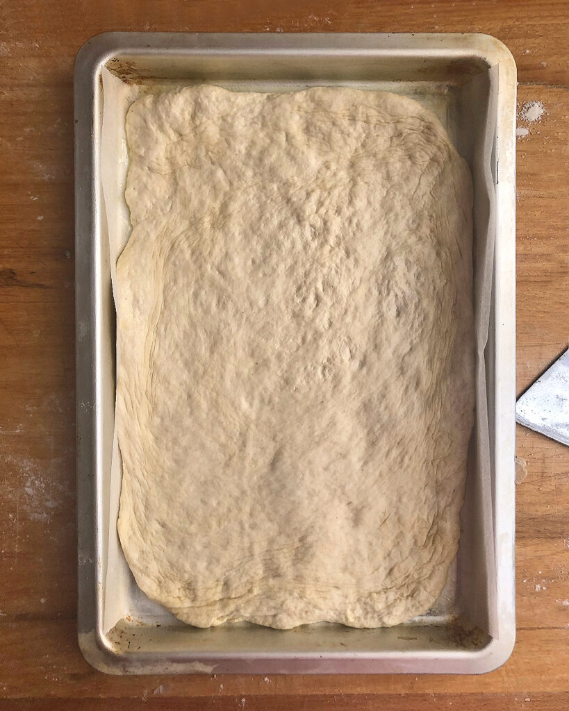 pizza dough sperad in a baking sheet