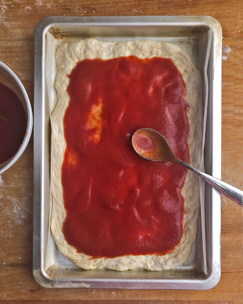 spreading tomato sauce on the pizza dough