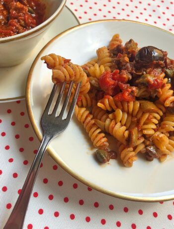 fusilli alla puttanesca served on a white dish with sauce on a side