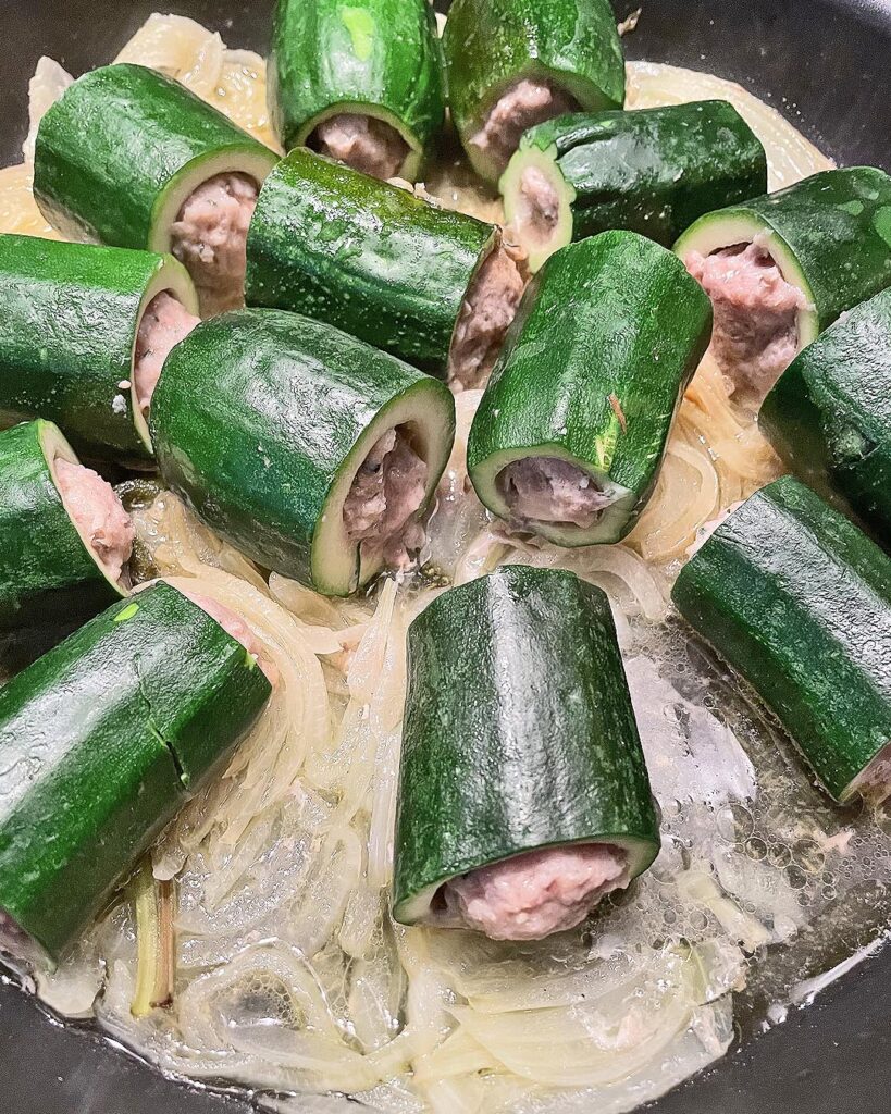 stuffed zucchini cooking in a pan with onions